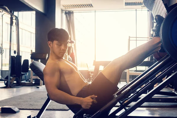Sporty asian young man work out heavy work on leg press machine