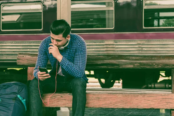 Genç adam akıllı telefon tutarak ve bekleme ile müzik çalma listesi kullanma