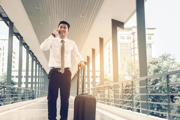 Bonito negócio asiático homem falando no móvel e segurando suitca — Fotografia de Stock