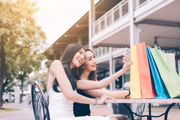 Shopping ragazze asiatiche seduti al di fuori del centro commerciale e utilizzando intelligente — Foto Stock