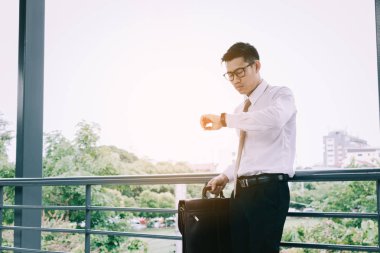 Zaman kontrol ve Evrak Çantası'nı tutan genç Asyalı erkek ayakta wi