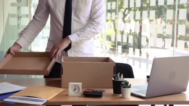 職場のテーブルの近くに立つ若い男性従業員退職後にカートンボックスの持ち物から彼のものを置く会社を離れる — ストック動画