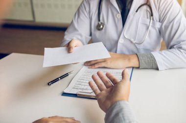 Asyalı erkek doktor klinik odasında konuşuyor ve bir önyazı teslim
