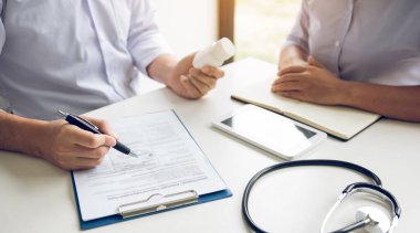 Kendine güveni tam bir doktor elinde bir ilaç şişesi, kıdemli bir hastayla konuşurken yazı yazıyor ve muayenehanede ilaçlarını gözden geçiriyor..