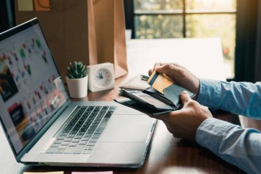 Asyalı adam, bilgisayardan online alışveriş yapmak için cebinden bir kredi kartı çıkarıyor..