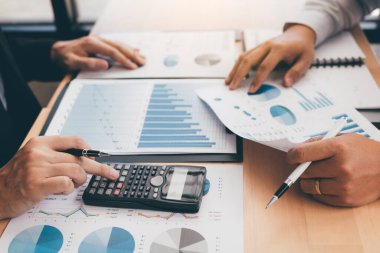 İki iş adamı, işletme işletme giderlerinin özet grafik raporlarını analiz ediyor ve ofisteki hesap makinesi kar hesaplamasını kullanıyor..