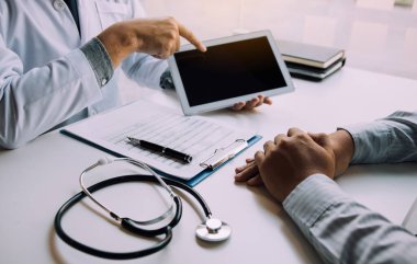 Hastanın durumunu ve tedavi sonuçlarını açıklayan tableti kullanırken Asyalı doktor hastayla konuşuyor..