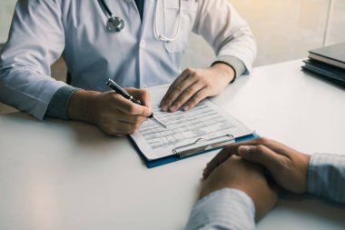 Doktor eli kalem tutuyor ve hastayla ilaç ve tedavi hakkında konuşuyor..