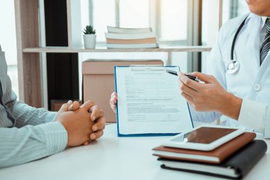 Kendine güvenen kadın doktor hastanın tıbbi bilgilerini inceler ve tıbbi formlara işaret eder..