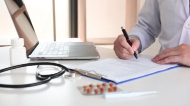 Doktorlar hasta hastalık raporları hakkındaki belgeleri okuyor ve bilgi kaydetmek için dizüstü bilgisayar kullanıyorlar.