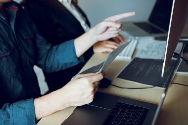 İki yazılım geliştiricisi ofis masasındaki ortağıyla birlikte çalışmak için bilgisayarları kullanıyor..