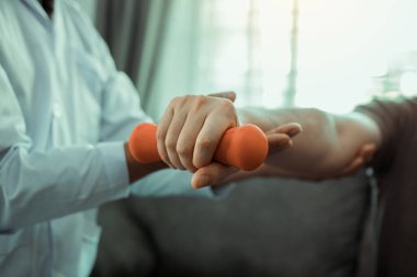 Asyalı fizyoterapistler, hastaların onun rehabilitasyonu yoluyla dambıllarını kaldırmalarına yardım ediyor..