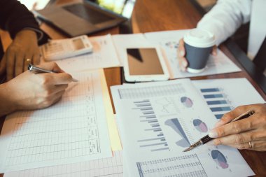 Bir grup işadamı, işletme işletme giderleri ve şirketin mali durumuyla ilgili çalışma verilerinin özet grafik raporlarını analiz ediyor..