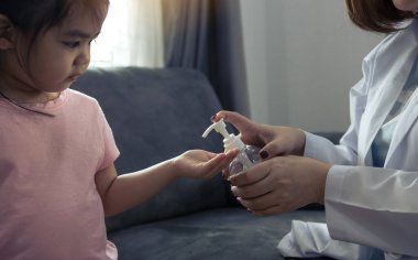 Kadın pediyatrist, Coronavirus salgını sırasında çocukların bakterilerini ve mikroplarını temizlemek için bir şişe alkollü el dezenfektanı tutuyor..