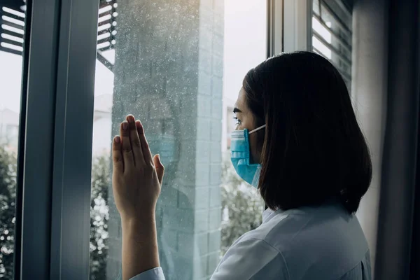 窓を通して見て 隔離された隔離されたままで病気から医療マスク保護を身に着けているアジアの女性Covid 19パンデミックウイルスマスク自宅でコロナウイルス病に対するマスク — ストック写真