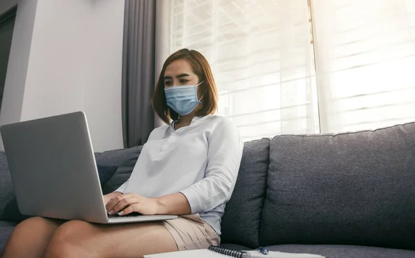 隔離と医療マスクを着用してコロナウイルスの流行中にラップトップコンピュータで自宅から働くアジアの女性 — ストック写真