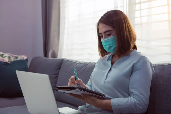 隔離と医療マスクを着用してコロナウイルスの流行中にラップトップコンピュータで自宅から働くアジアの女性 — ストック写真