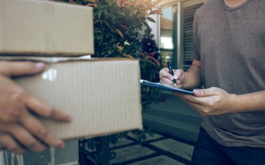Evinin kapısında duran teslimatçı genç adam ve genç bir erkeğin imzalaması için paketler taşıyor..