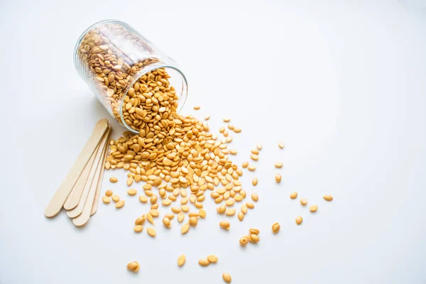 Beyaz arka planda altın balmumu ve tüy dökmek için tahta çubuklarla dolu cam bir kavanoz var..