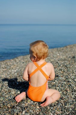 Küçük kız onu geri dönme ve seyir sahilde oturuyor