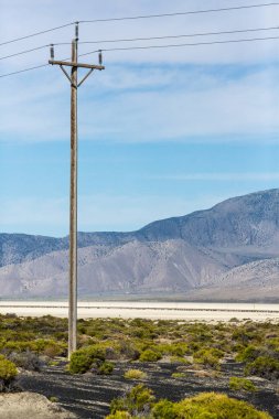 Elektrik hatları mavi gökyüzüne karşı siyah kaya çölü Nevada 'nın yanında.