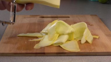 Peeling strips of yellow summer squash into a pile on a cutting board