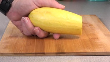Peeling thin slices off of a yellow summer squash over a cutting board