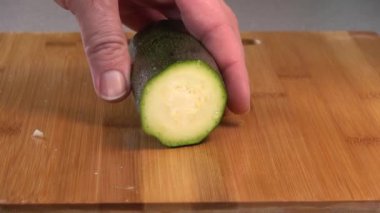  Slicing a green zucchini with an peeler on a wood cutting board.