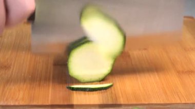 Chopping a green zucchini with a cleaver on a wood cutting board