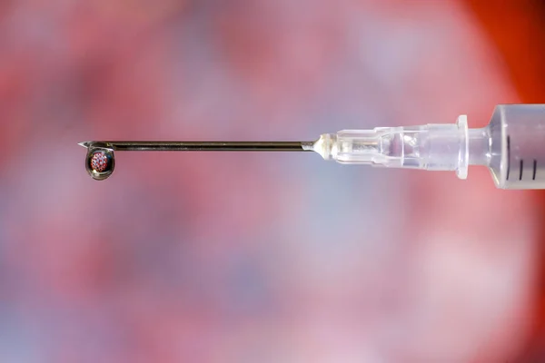 Hypodermic needle dripping fluid over a red and grey out of focus background