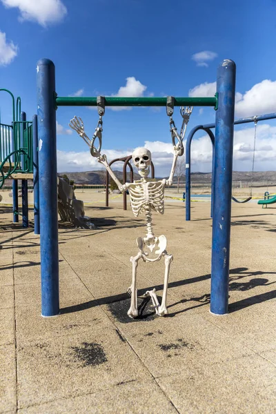 Skeleton playing on a child\'s hanging toy in an empty park