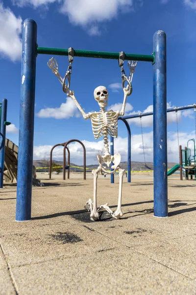 Skeleton playing on a child\'s hanging toy in an empty park