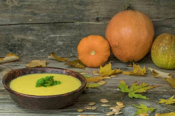 Winter Pumpkin Cream Soup in hand made ceramic plate on rustic old wooden background with autumn maple leaves and small squash. Vegan nutritional food. — Stock Photo, Image
