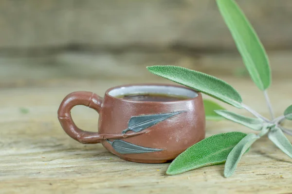 Natural therapeutic healing herbal anti-inflammatory, antimicrobial and tonic sage tea in small chinese ceramic cup  with fresh green leaves. Flu cold winter days. Herbal medicine.