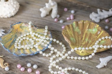İncili el yapımı seramik kabuk. Eski ahşap arka plan üzerinde inci mercan, inci kabuğu, inci boncuklar, deniz temalı kompozisyon. Kadın iğne işi el işi aksesuarlar kavramı