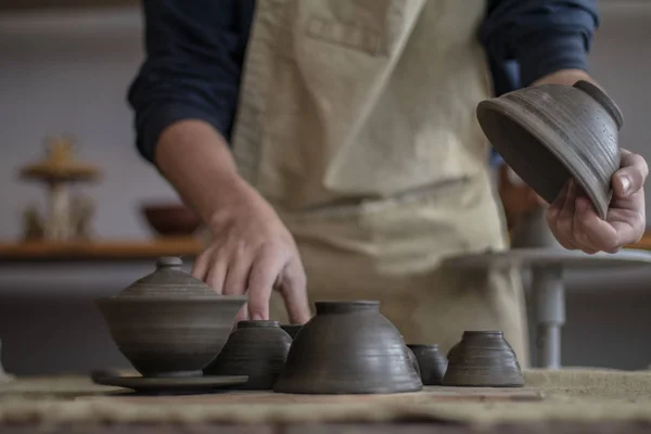 Joven alfarero sucio en manos de barro sosteniendo una taza de cerámica que se hizo a sí mismo en la rueda alfarera en la escuela de cerámica. Arte y negocios, hobby y concepto de trabajo freelance. Enfoque selectivo . Fotos De Stock Sin Royalties Gratis