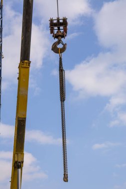 Vinç kancası ve zinciri bulutlu mavi gökyüzüne asılı. İnşaat konuları. siyah ve sarı mobil (kamyon vinci) vinç bom