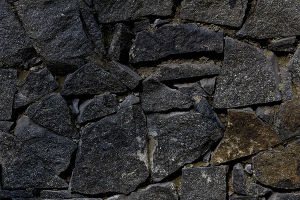 stone fence. fence of black stones of irregular shape. a fence of chipped stones. stone texture.