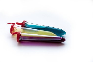 Beyaz zemin üzerinde kırmızı, sarı ve mavi sıvı bulunan üç test tüpü. Test tüplerindeki madde virüs için bir ilaç ya da aşıya benziyor. Fotoğrafın teması: Coronavirüs salgınları (COVID-19). İzole edilmiş resim.