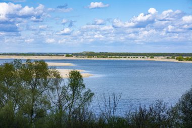 Güzel manzara. Bulutlu mavi gökyüzü, tepeden göle manzara, çevrede yeşil ağaçlar. Bahar güneşli gün.