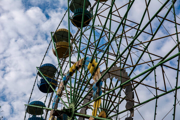Vintage old ferris wheel in blue and yellow against the blue sky and white clouds.