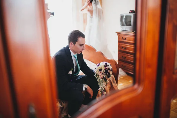 Prachtige lachende bruidegom. Knappe man in een suite met een knoopsgat zittend op de vensterbank binnen — Stockfoto