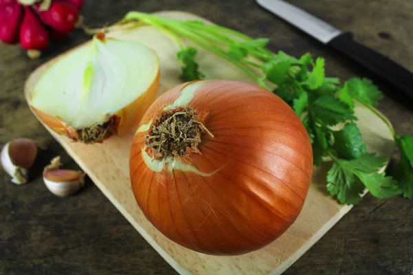 Whole and sliced onions on wooden cutting board — Stock Photo, Image