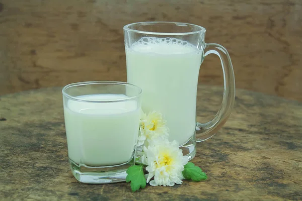 En flaska mjölk och glas mjölk på ett träbord på en bakgrund — Stockfoto