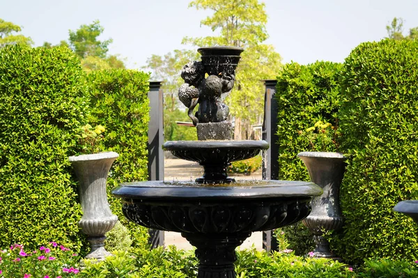 Jardín con pequeña fuente y banco de piedra verde césped plantas árboles arbustos —  Fotos de Stock