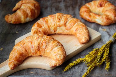 Ahşap kesme tahtasının üstünde taze pişmiş kruvasanlar.