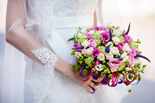 Noiva em vestido e véu nupcial mantém buquê de casamento — Fotografia de Stock