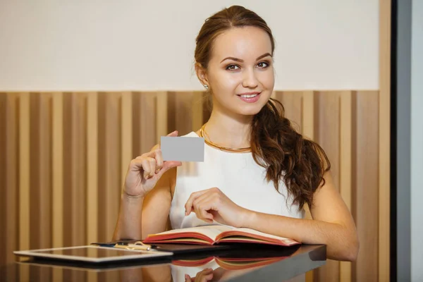 Молодая женщина стоит у стола и держит визитную карточку — стоковое фото