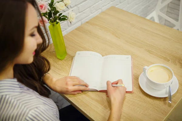Pretty smiling woman makes entry in her diary on table — Stock Photo, Image