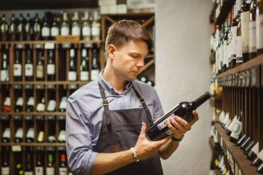Genç sommelier şişe kırmızı şarap mahzeninde tutuyor